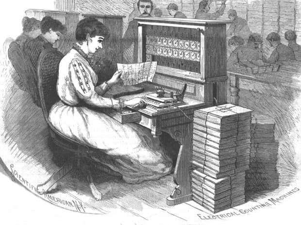 Greyscale engraving of a woman seated at a Hollerith tabulating machine, reading a census schedule beside a wall of counting dials, with tied bundles of paper stacked on the floor and clerks working behind her.